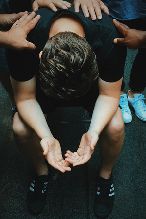 man leans elbows on knees people place hands on back